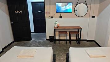 Habitación de hotel con dos camas, un escritorio con televisor, un espejo y una puerta con la etiqueta A605.