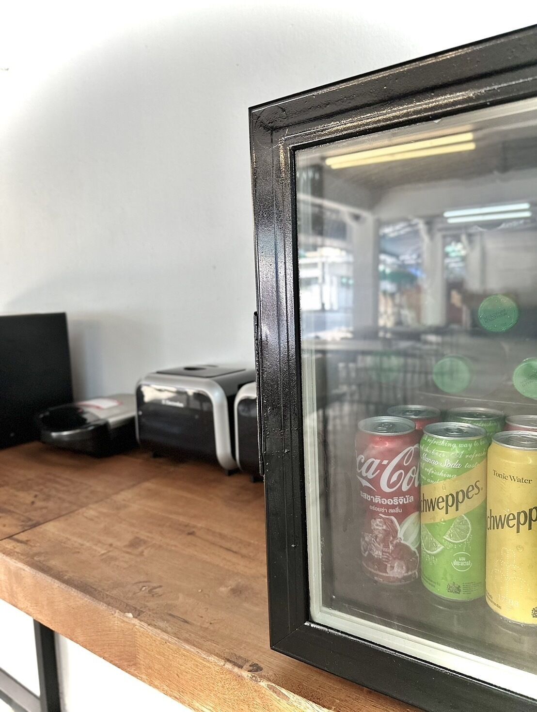 Una teca incorniciata contenente lattine di Coca-Cola, Schweppes e acqua tonica.