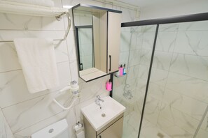 A bathroom with a white sink, a mirror, a towel rack, and a shower enclosure.