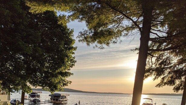 A grassy area with a picnic table and a grill, overlooking a body of water with boats and a dock. - Classic Green Lake cottage, lakefront, screened boathouse deck, dock, swimming (Markesan)