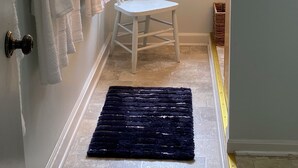 A bathroom with a white chair, a black rug, and a window with greenery outside. - Classic Green Lake cottage, lakefront, screened boathouse deck, dock, swimming (Markesan)