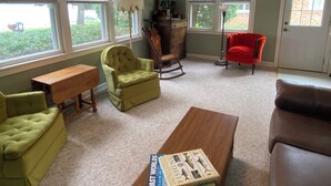 A living room with a ceiling fan, green and red chairs, a wooden coffee table, and a bookshelf. - Classic Green Lake cottage, lakefront, screened boathouse deck, dock, swimming (Markesan)