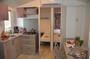 Une cuisine de taille réduite, dotée de meubles en bois, d’une cuisinière à gaz et d’un évier. On aperçoit un petit coin repas avec une table et des chaises.