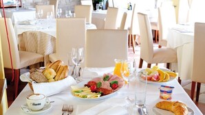 Un desayuno con cruasanes, pan, una fuente de embutidos y quesos, fruta y una taza de café con la etiqueta "Monte".