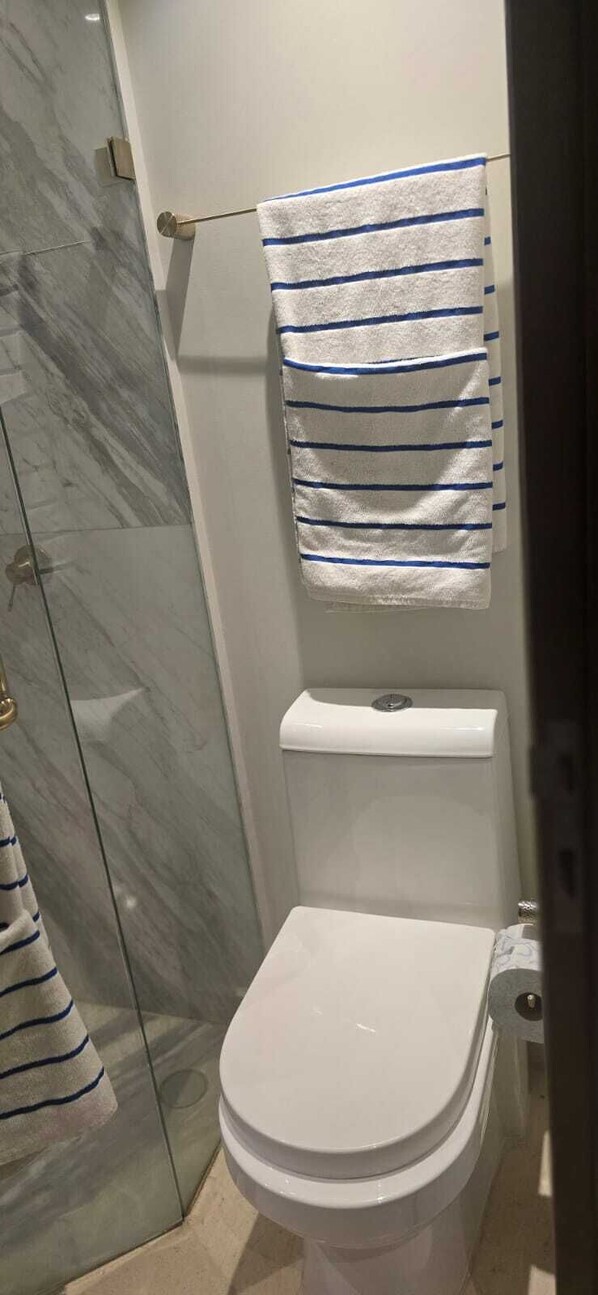 Un baño con inodoro, un perchero con toalla a rayas y suelo de mármol.