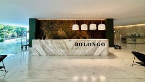 A reception desk with a marble top labeled "BOLONGO" in a modern lobby with a view of palm trees. - Park Life Bolongo (Bucerías)