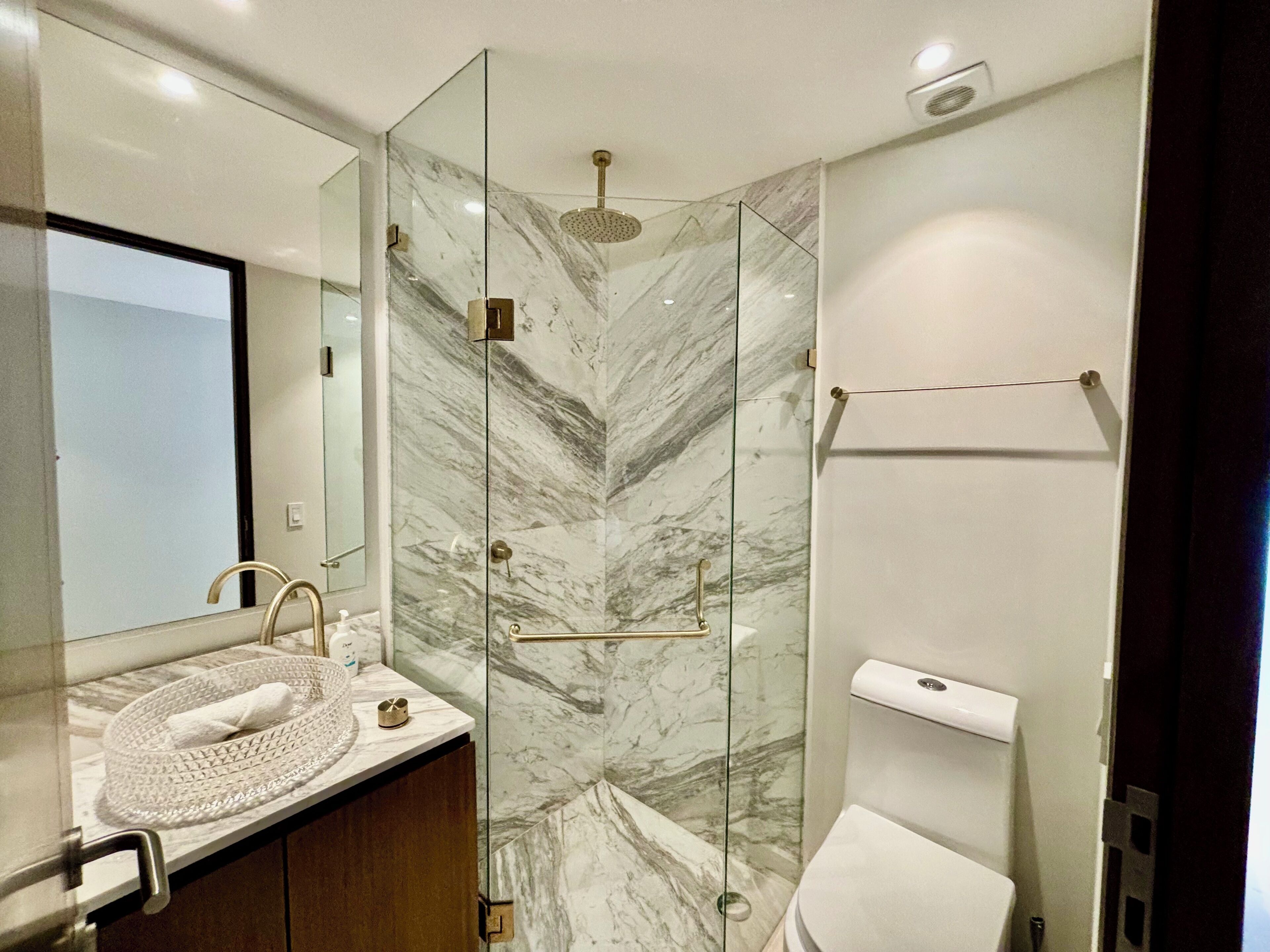 Un baño moderno con cabina de ducha de vidrio, salpicadero de mármol, lavamanos con toalla e inodoro.
