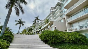 A modern hotel with a staircase leading to a multi-level building, surrounded by palm trees and greenery. - Park Life Bolongo (Bucerías)