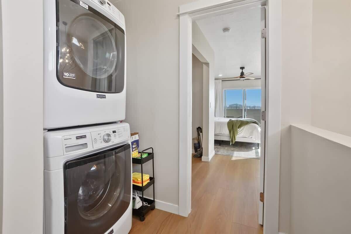 A laundry room with stacked washers and dryers, a cart with cleaning supplies, and a view of a balcony with a table and chairs.
