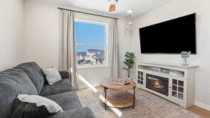 A living room with a grey sofa, a round wooden coffee table, a fireplace, and a TV mounted on the wall. - Private Caldwell Guesthouse w/ King Bed, Balcony & Kitchenette (Caldwell)