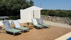 A poolside area with lounge chairs and a table, surrounded by a wooden deck and a stone wall. - Modern Villa 6 pax, private pool, countryside views, free wifi (Binibeca)