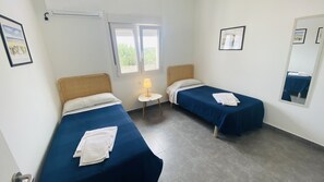 A room with two single beds, a small table with a lamp, and a window with blinds. - Modern Villa 6 pax, private pool, countryside views, free wifi (Binibeca)