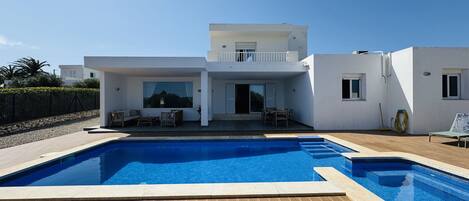 Una casa moderna de dos pisos con piscina, mobiliario exterior y una vista despejada del cielo.