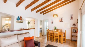 Un salon moderne avec un canapé, une table basse, une table à manger en bois et des chaises. On aperçoit un coin cuisine au fond.