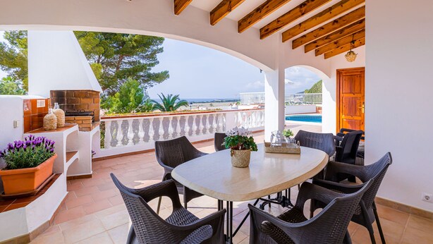 Une terrasse extérieure avec une table ronde et des chaises en osier, donnant sur une piscine et offrant une vue panoramique.