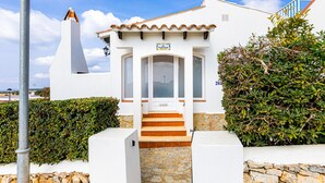 Un bâtiment blanc avec un toit en tuiles et une cheminée, doté d’un escalier menant à une porte au-dessus de laquelle est apposée une enseigne.