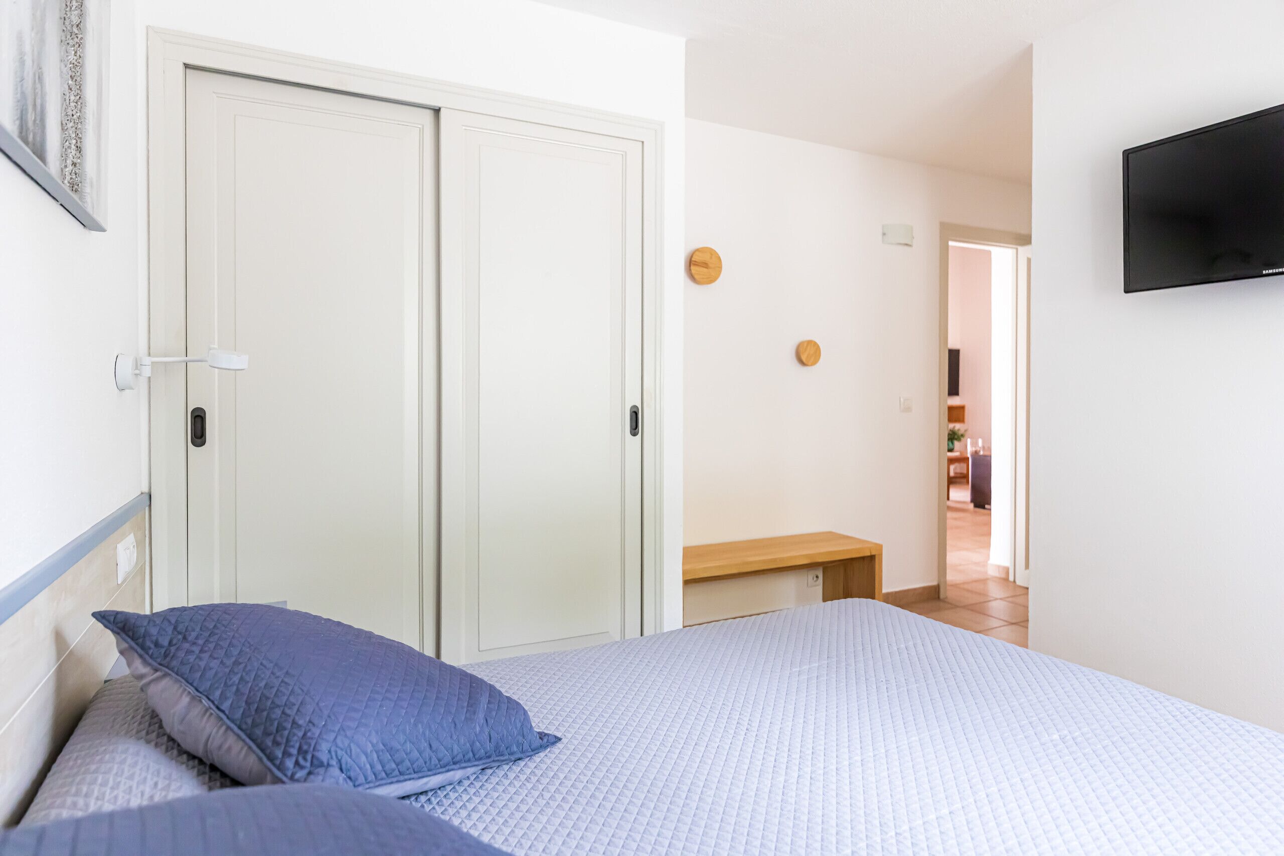 Un dormitorio con una cama, un banco y un televisor montado en la pared.