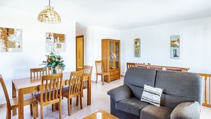 Un salon avec un canapé gris, une table à manger en bois et des chaises. On y trouve un meuble avec des portes en verre et un luminaire suspendu.