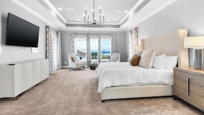 A modern bedroom with a large bed, a TV, a chandelier, and a view of the ocean.