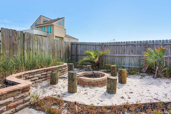 A backyard with a wooden fence, a brick fire pit, and a palm tree. - 🏝️ Fathom Resort – Sleeps 20, Saltwater Pool, Elevator + Gulf Views (Pensacola Beach)