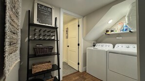 A laundry room with a washing machine and dryer, a shelf with baskets, and a chalkboard sign. - Charming 1 bed/bath Suite in waterfront Cottage (Somers)