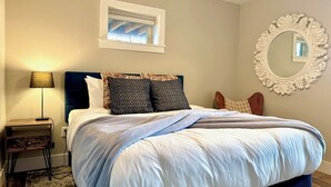 A bedroom with a bed, bedside table, lamp, window, and decorative mirror. - Charming 1 bed/bath Suite in waterfront Cottage (Somers)