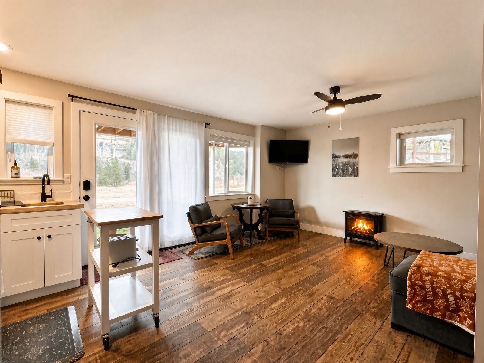 A cozy living room with a fireplace, wooden flooring, a ceiling fan, and a TV mounted on the wall.