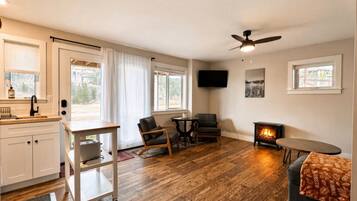 A cozy living room with a fireplace, wooden flooring, a ceiling fan, and a TV mounted on the wall.