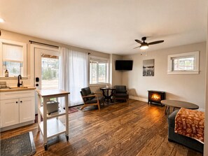 A cozy living room with a fireplace, wooden flooring, a ceiling fan, and a TV mounted on the wall.
