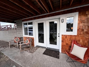 A covered porch with a wooden bench and a leather chair, a white door with glass panels, and a brick wall.