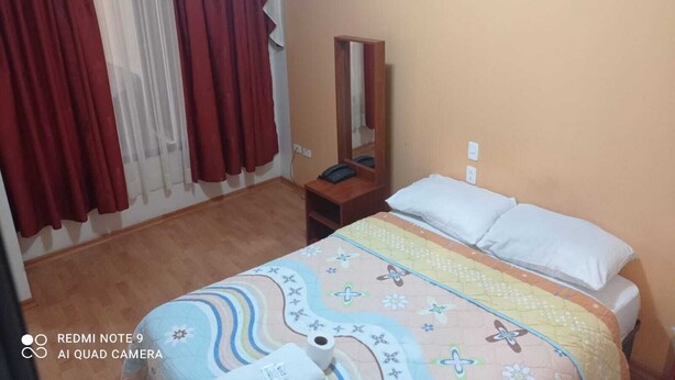 A bedroom with a bed, a bedside table, a mirror, and a window with red curtains.