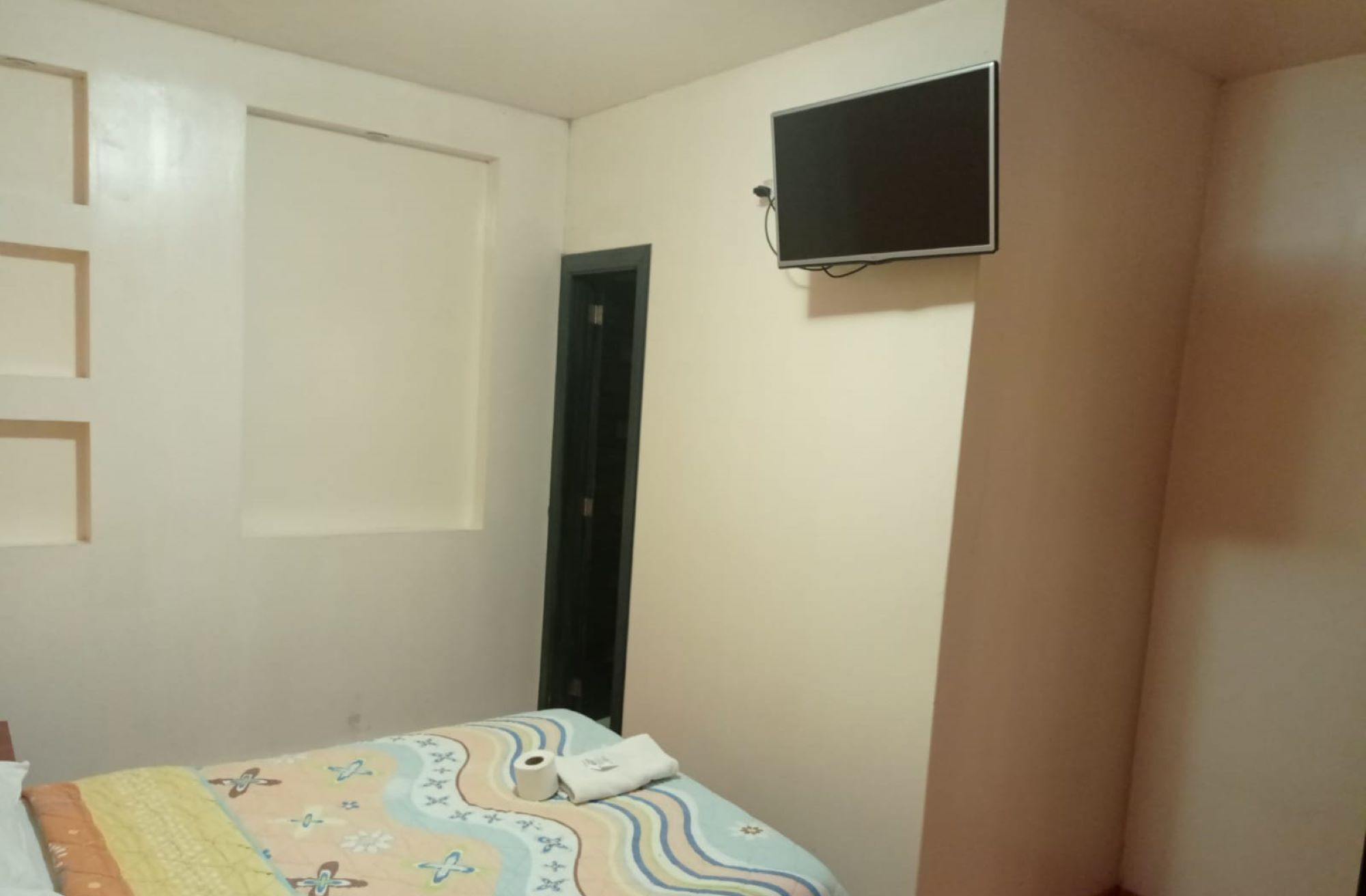 Un dormitorio con una cama, una puerta y un televisor montado en la pared.