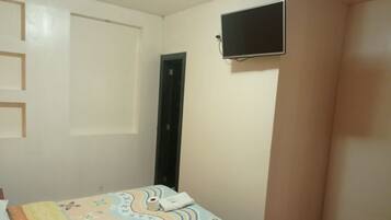 Un dormitorio con una cama, una puerta y un televisor montado en la pared.