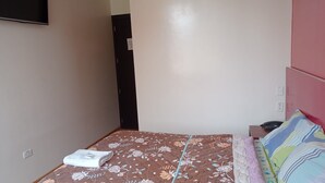 A bedroom with a bed, a bedside table, a wall-mounted TV, and a door.