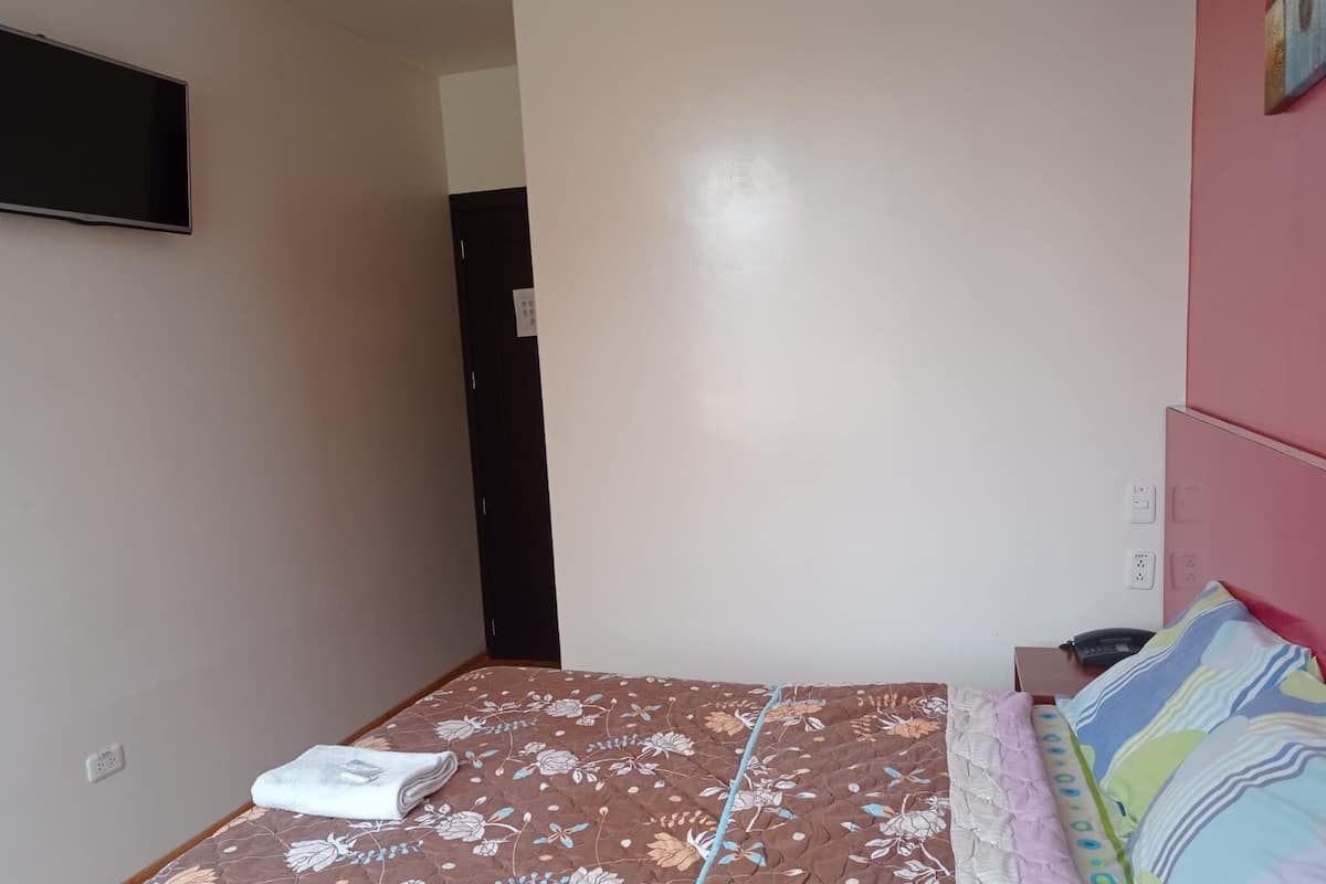 A bedroom with a bed, a bedside table, a wall-mounted TV, and a door.