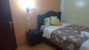A bedroom with a bed, a nightstand, a wall socket, and a door.