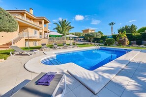 A swimming pool with lounge chairs and a sunbed, surrounded by a landscaped garden and a multi-story building.