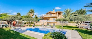 A two-story house with a swimming pool, surrounded by greenery and palm trees.