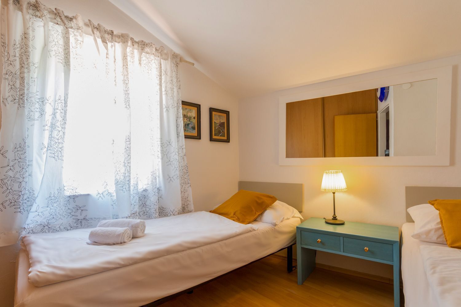Hotellihuone, jossa on yksi sänky, yöpöytä lampun kanssa, pieni pöytä ja peili seinällä.