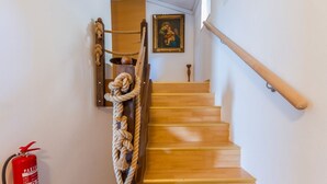 Una escalera de madera con barandilla de cuerda, un cuadro enmarcado en la pared y un extintor en la pared.