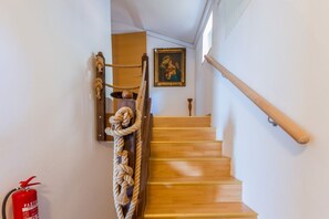 A wooden staircase with a rope handrail, a framed painting on the wall, and a fire extinguisher on the wall.
