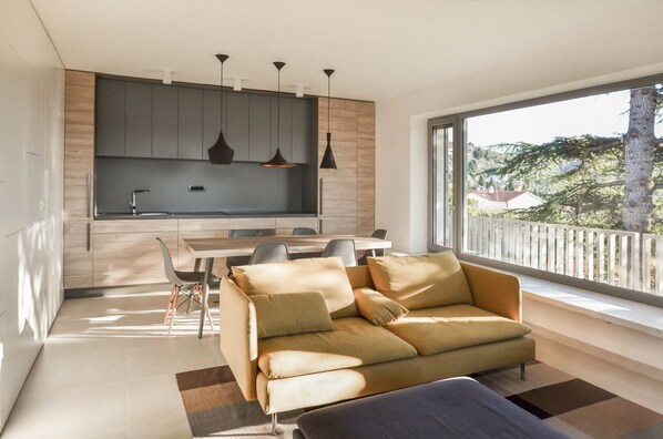 A modern living room with a sofa, a dining table, and a kitchen area with cabinets and pendant lights.