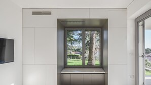 A modern room with a built-in bench, a large window with a view of trees and a lawn, and a flat-screen TV mounted on the wall.