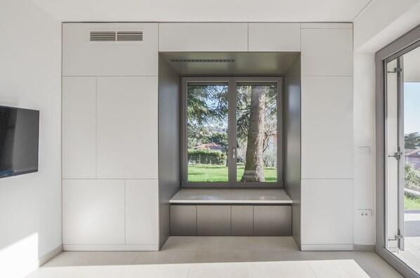 A modern room with a built-in bench, a large window with a view of trees and a lawn, and a flat-screen TV mounted on the wall.