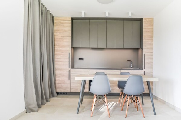A compact kitchen with a built-in stove, a sink, and a small countertop. There are two grey chairs and a white table.