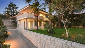 A two-story house with a balcony, a stone wall, and a well-maintained lawn.