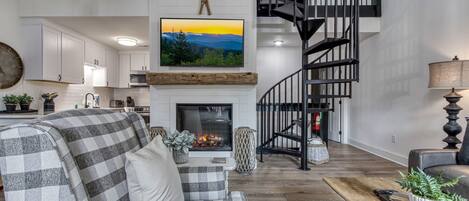 A modern living room with a fireplace, a checkered sofa, a coffee table, and a staircase leading to an upper level.