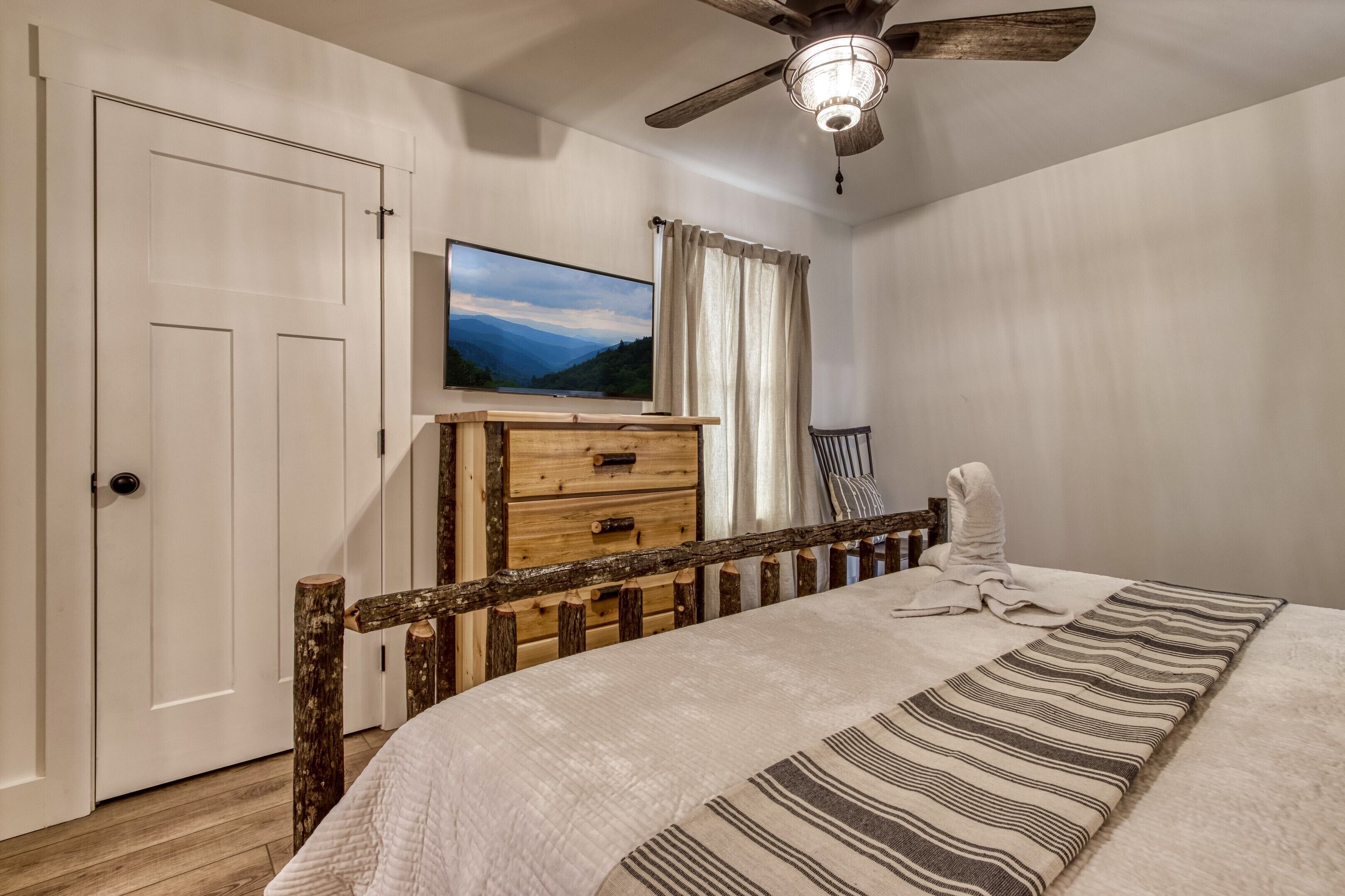 A bedroom with a bed, a wooden dresser, a television, and a ceiling fan.