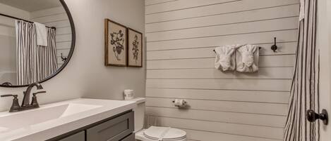 A bathroom with a white sink, a toilet, and a shower with striped curtains. There are framed pictures on the wall and a towel rack with towels.