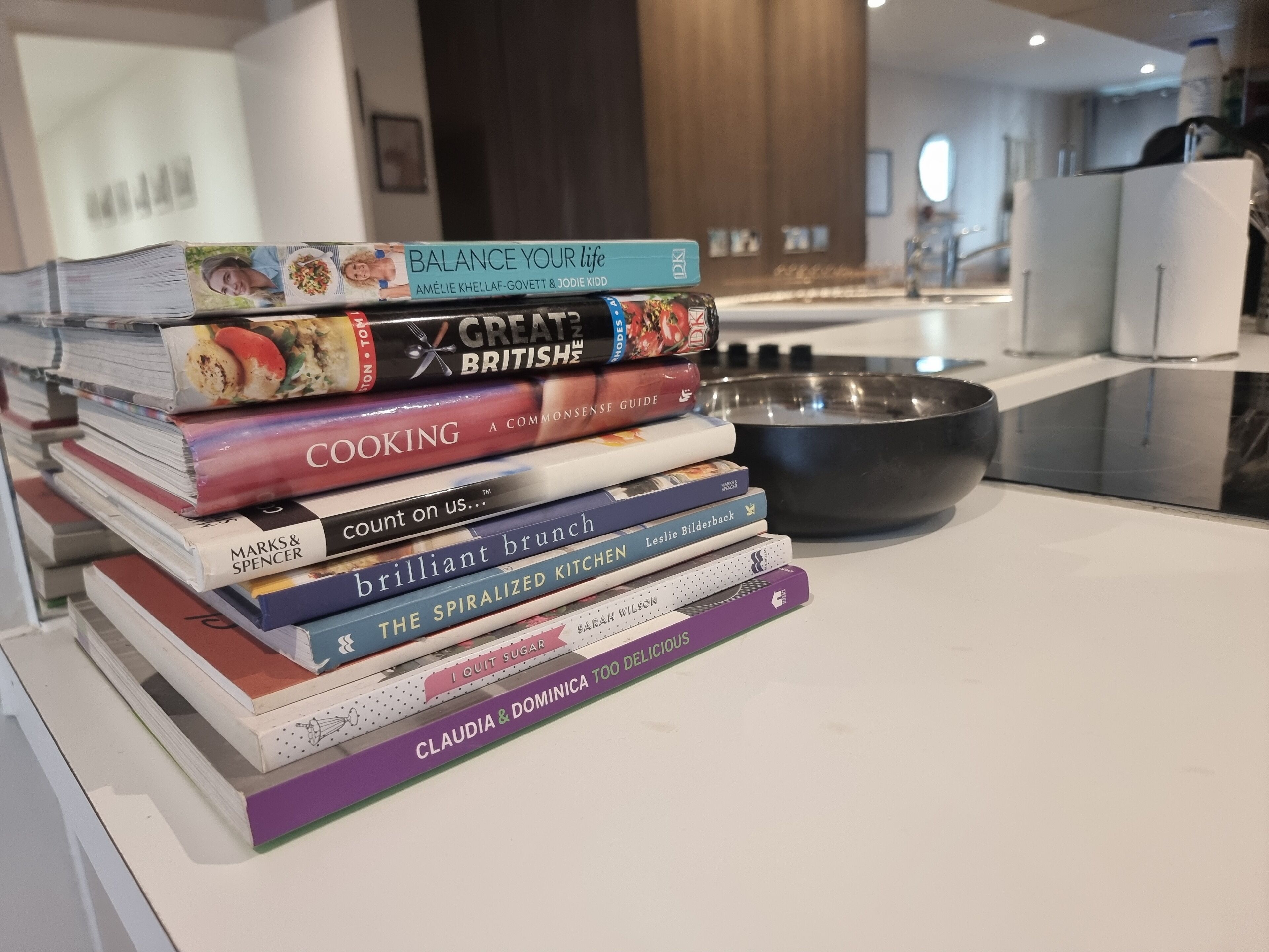 A stack of cookbooks on a kitchen counter with a large mixing bowl.